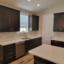 Kitchen featuring dark wood cabinetry, light countertops, a double basin stainless steel sink, a stainless steel dishwasher, and wood-finish flooring