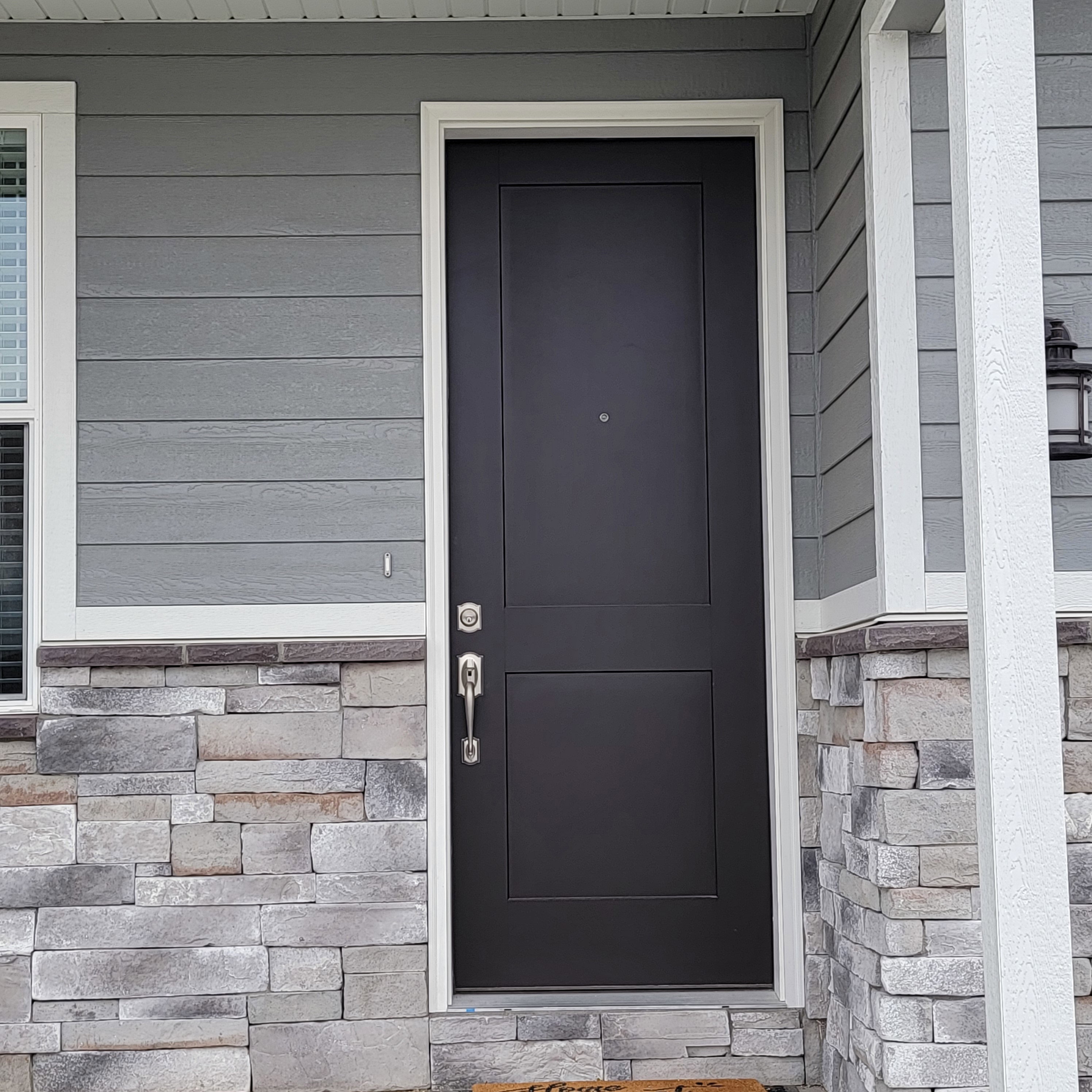 Modern black entry door with white trim, horizontal siding, and a stone facade