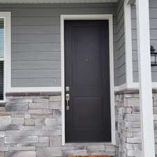 Modern black entry door with white trim, horizontal siding, and a stone facade