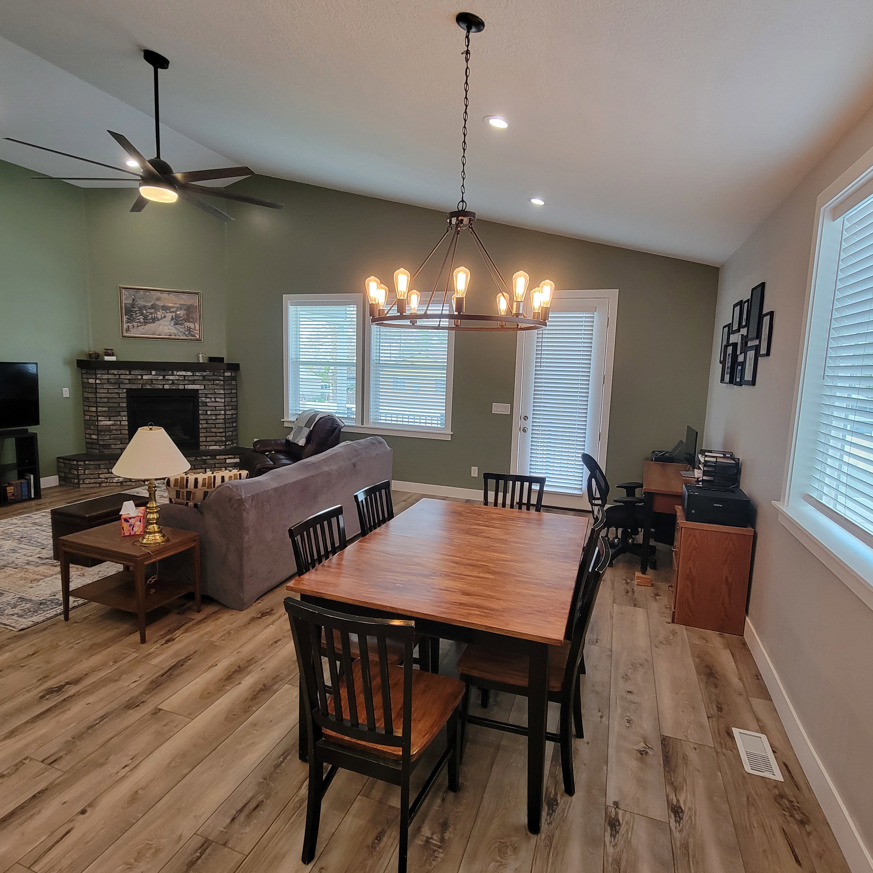 Open-concept living area featuring vaulted ceilings, wood-finish flooring, and a brick-surround fireplace