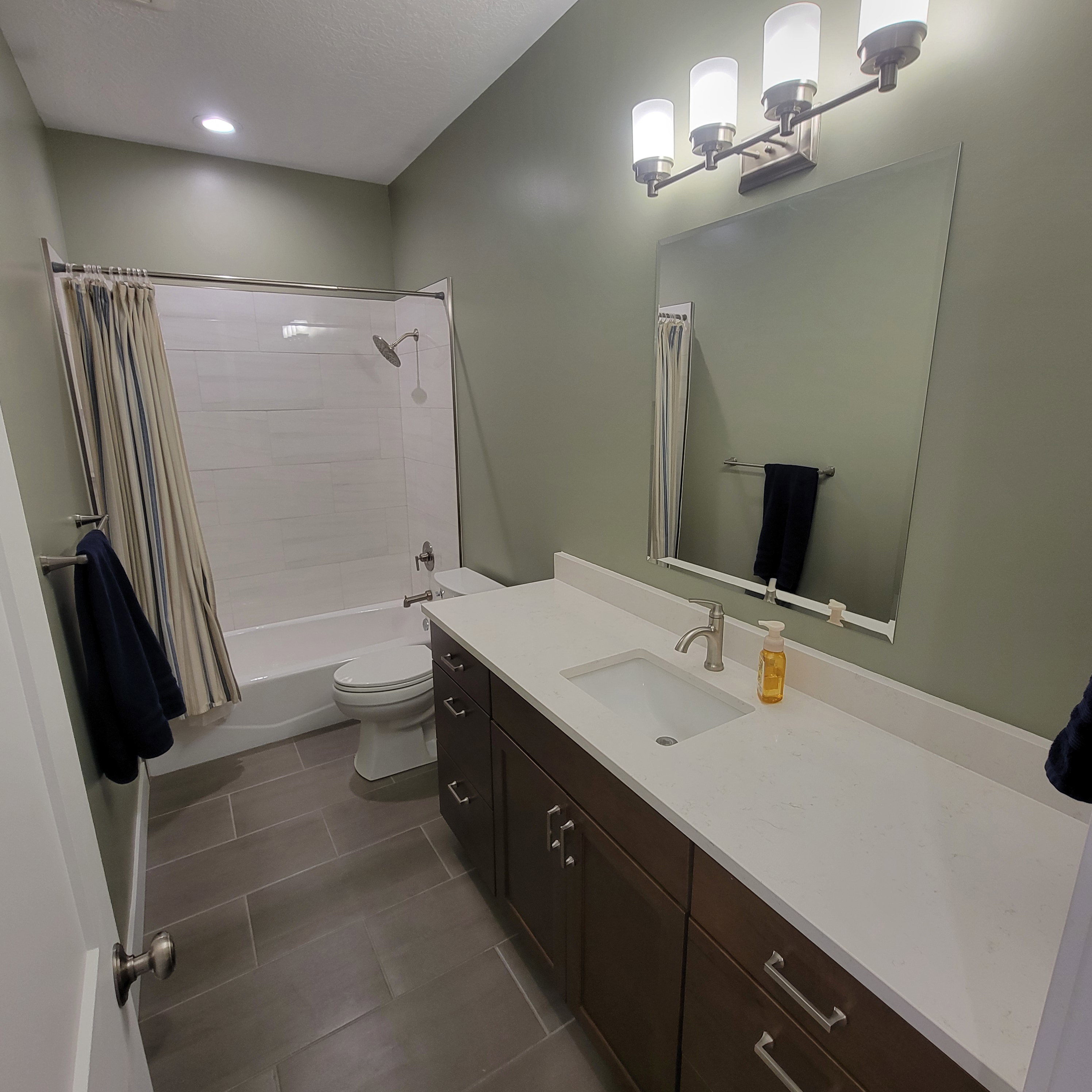 Modern bathroom featuring a single vanity with a white countertop and dark wood-finish cabinetry, a large wall-mounted mirror, and a three-light vanity fixture