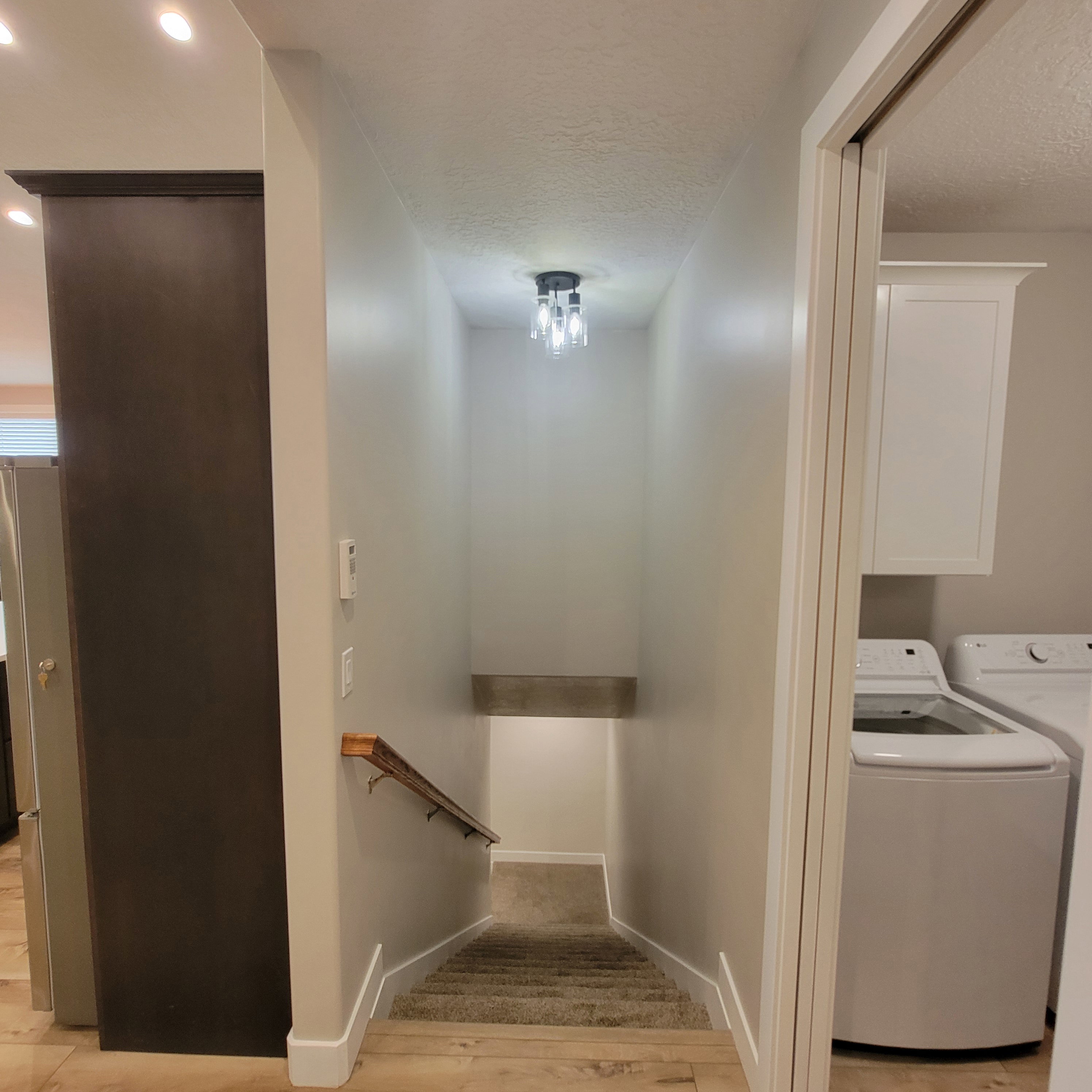 Stairwell featuring a contemporary ceiling-mounted light fixture, light gray walls, a wood handrail, and carpeted steps