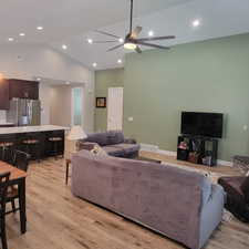 Open-concept living area featuring vaulted ceilings with recessed lighting, a large ceiling fan, wood-finish flooring, and a kitchen island with seating