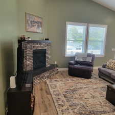 Living area featuring a brick fireplace with a dark mantel, wood-finish flooring, and vaulted ceilings