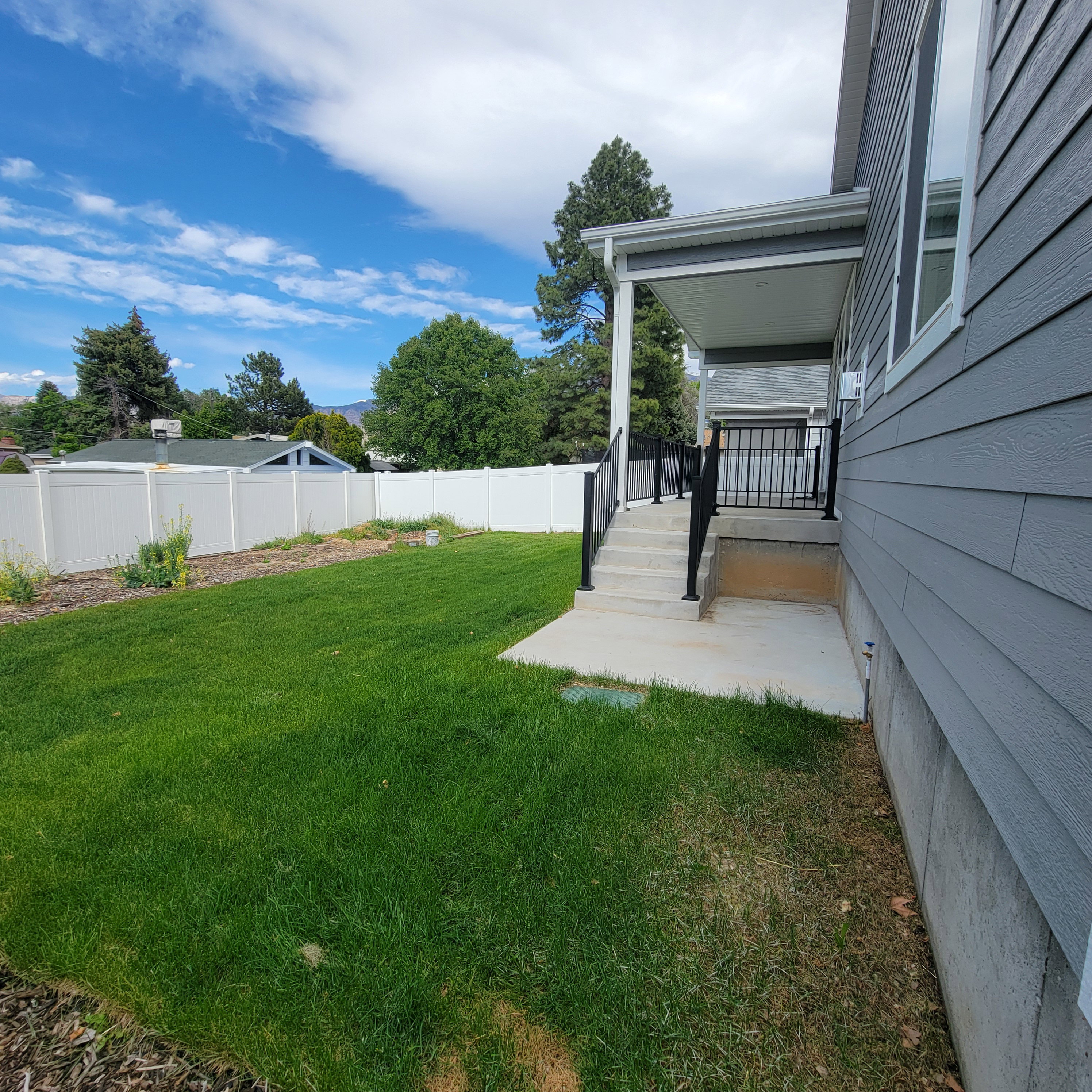 Spacious backyard with a vibrant green lawn, concrete patio, and a covered porch featuring dark metal railings