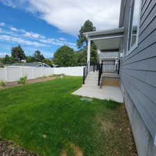 Spacious backyard with a vibrant green lawn, concrete patio, and a covered porch featuring dark metal railings