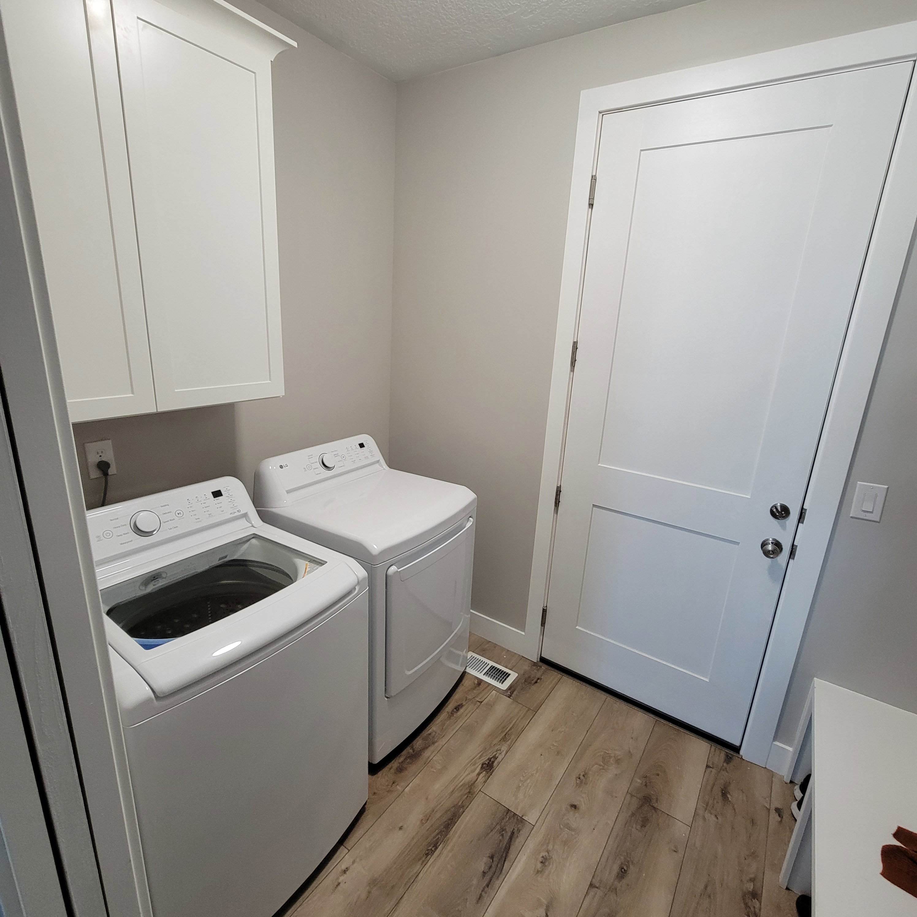 Dedicated laundry area featuring wood-finish flooring, light neutral wall paint, and overhead white cabinetry