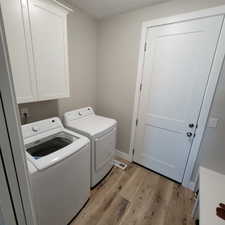 Dedicated laundry area featuring wood-finish flooring, light neutral wall paint, and overhead white cabinetry