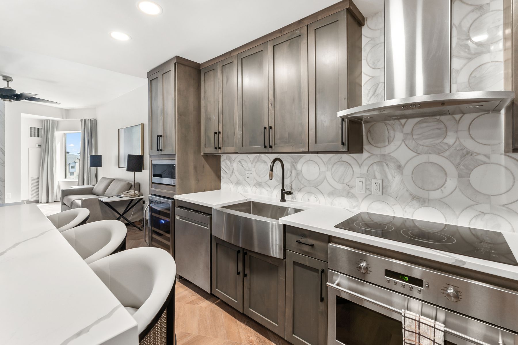 Contemporary kitchen featuring wood-finish cabinetry, stainless steel appliances, a large farmhouse sink, and a unique circular pattern backsplash