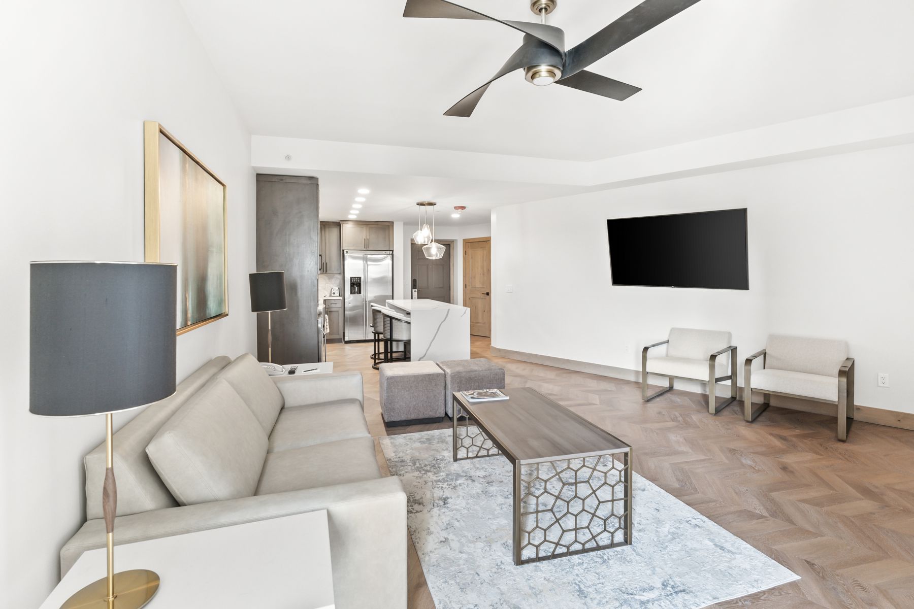 Open-concept living space featuring wood-finish flooring in a herringbone pattern and a contemporary ceiling fan
