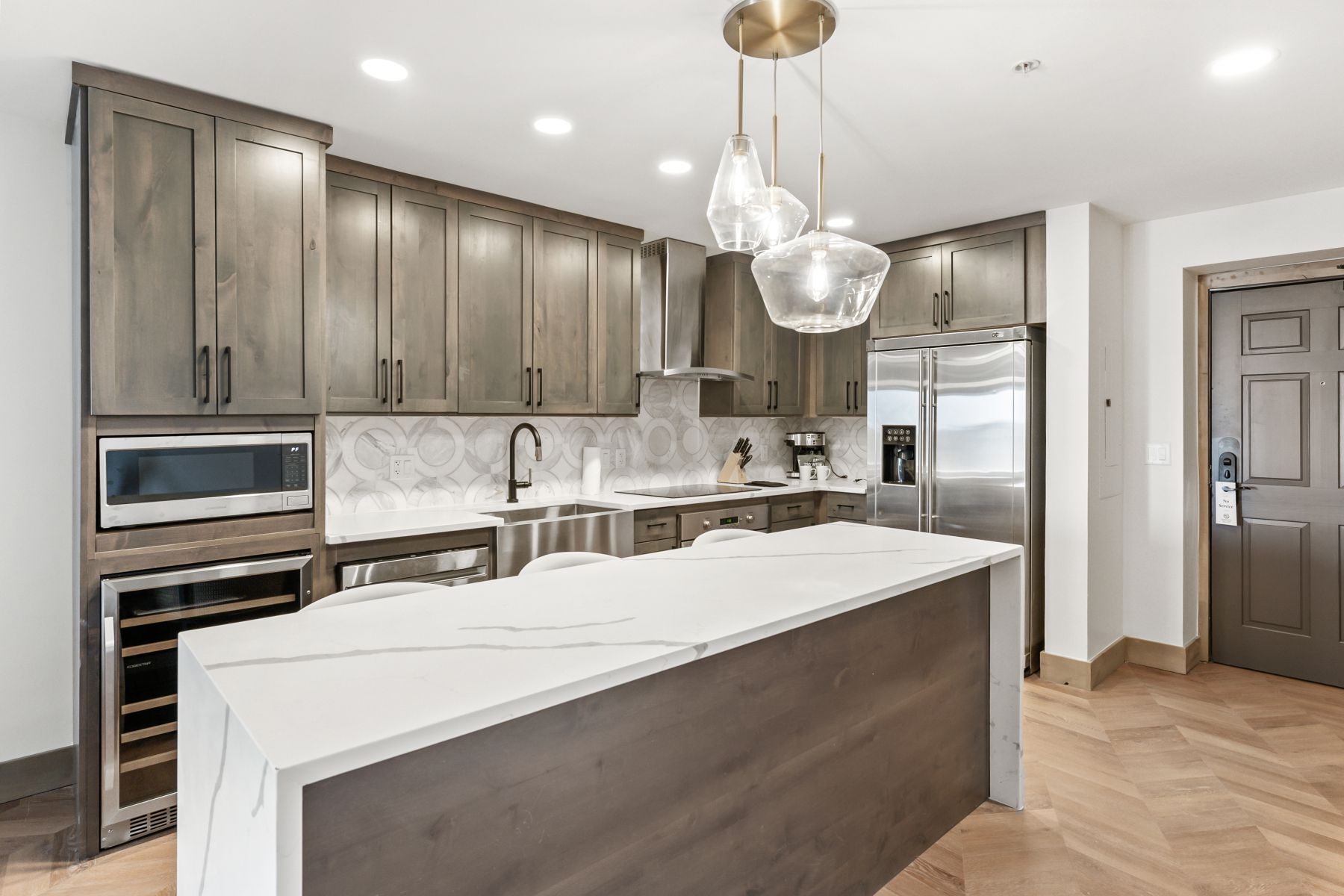 Kitchen featuring a waterfall island with a quartz countertop, wood-finish cabinetry, stainless steel appliances, and herringbone-pattern wood-finish flooring