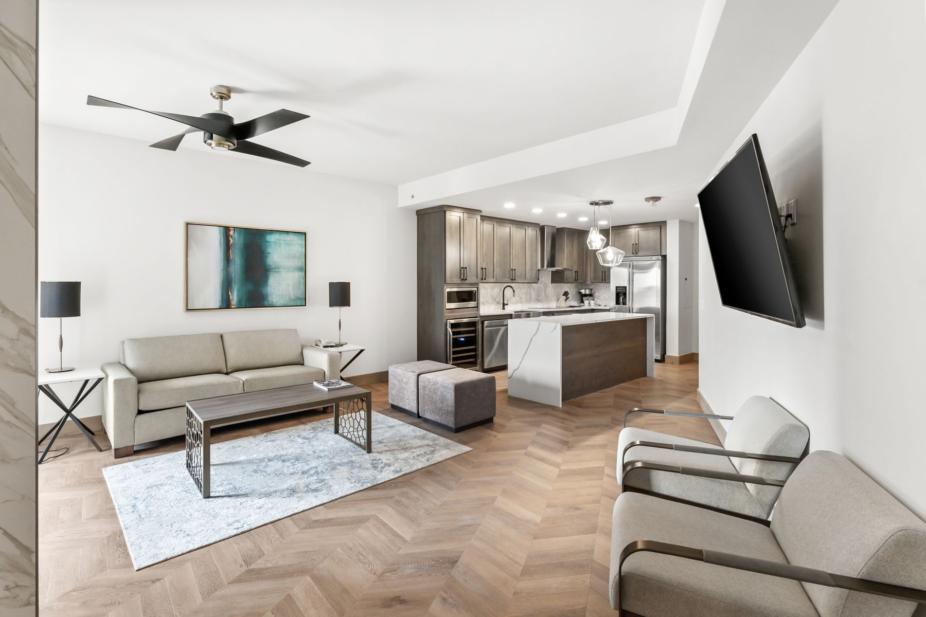 Open-concept living space featuring herringbone wood-finish flooring, a modern ceiling fan, recessed lighting, a kitchen island with a waterfall countertop, and stainless steel appliances
