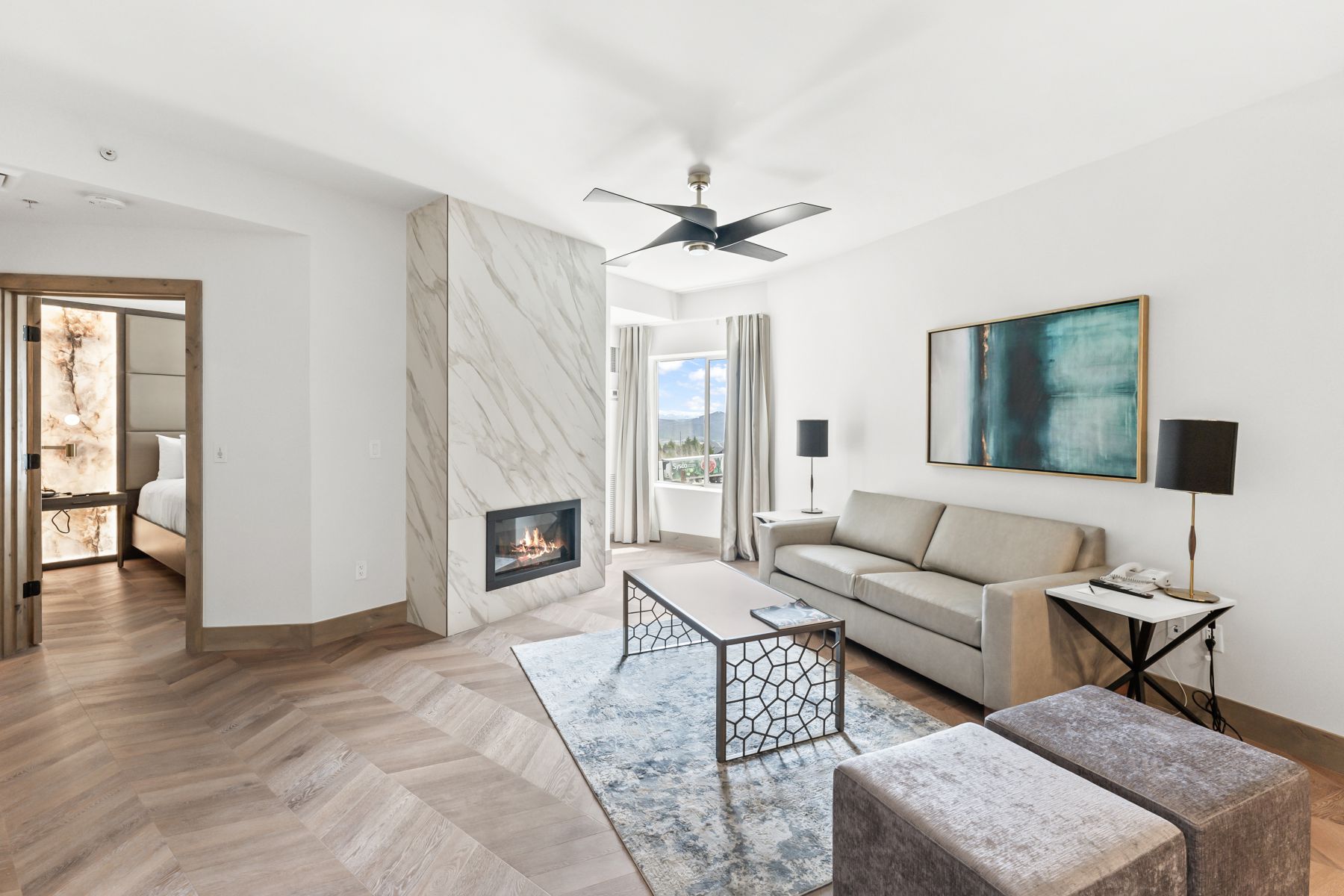 Spacious living area featuring herringbone wood-finish flooring, a contemporary fireplace with a marble-look surround, a ceiling fan, and large windows with mountain scenery