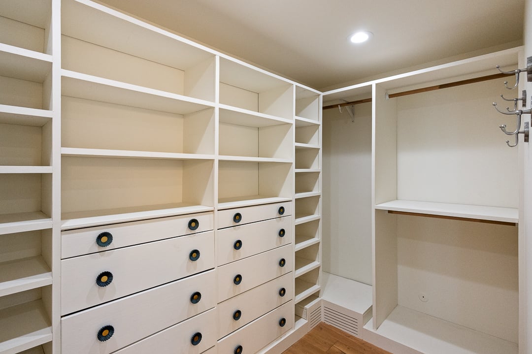 Custom closet system featuring extensive shelving, multiple drawers with decorative hardware, hanging rods, and wood-finish flooring