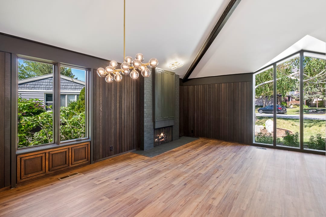 Spacious room featuring wood-finish flooring, a contemporary chandelier, a built-in fireplace with a dark surround, and large windows with dark framing
