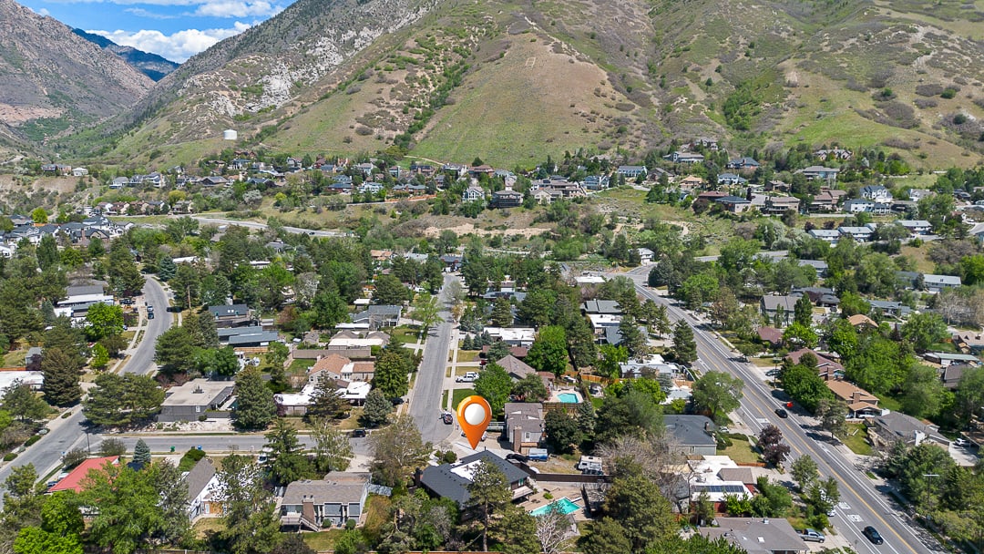 Aerial perspective showcasing a residential neighborhood with mature trees and mountainous terrain in the background