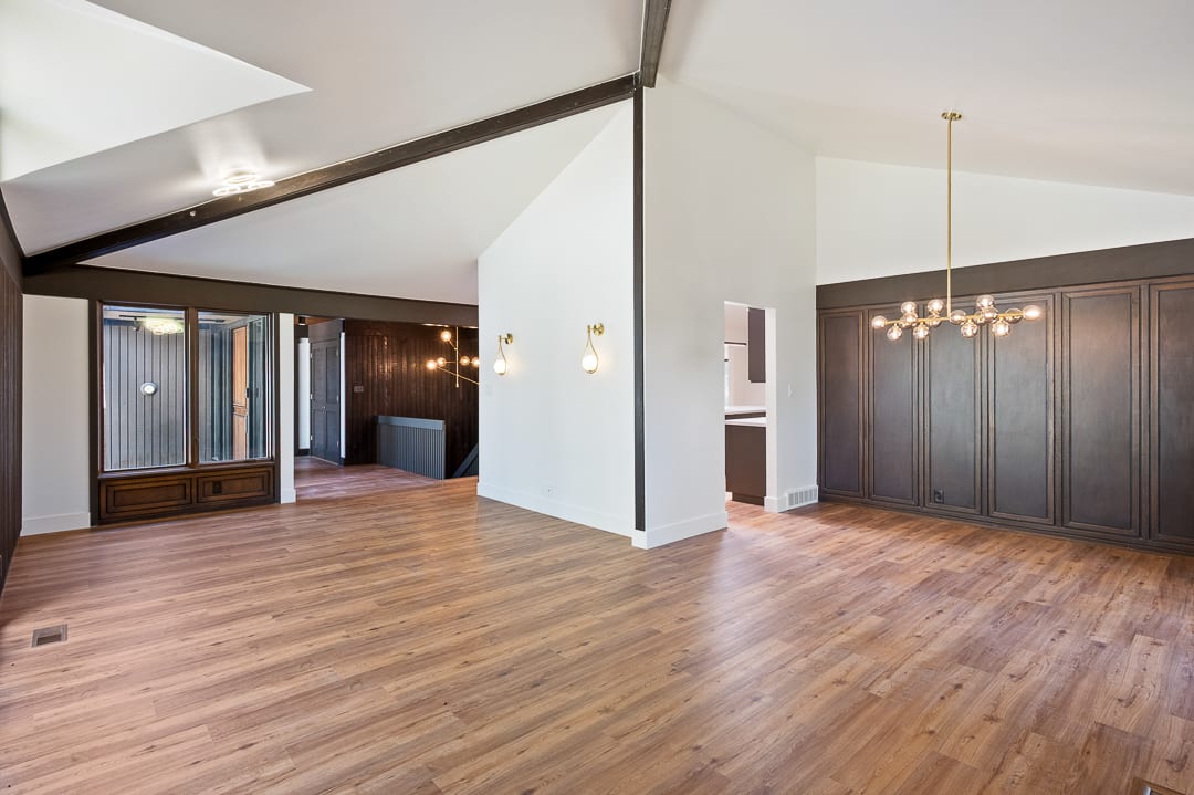 Spacious open-concept room featuring vaulted ceilings, wood-finish flooring, a contemporary linear chandelier, and integrated wall paneling
