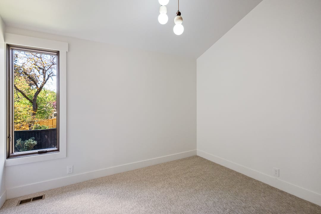 Room featuring a large vertical window, light beige carpeting, white walls, and bright overhead lighting
