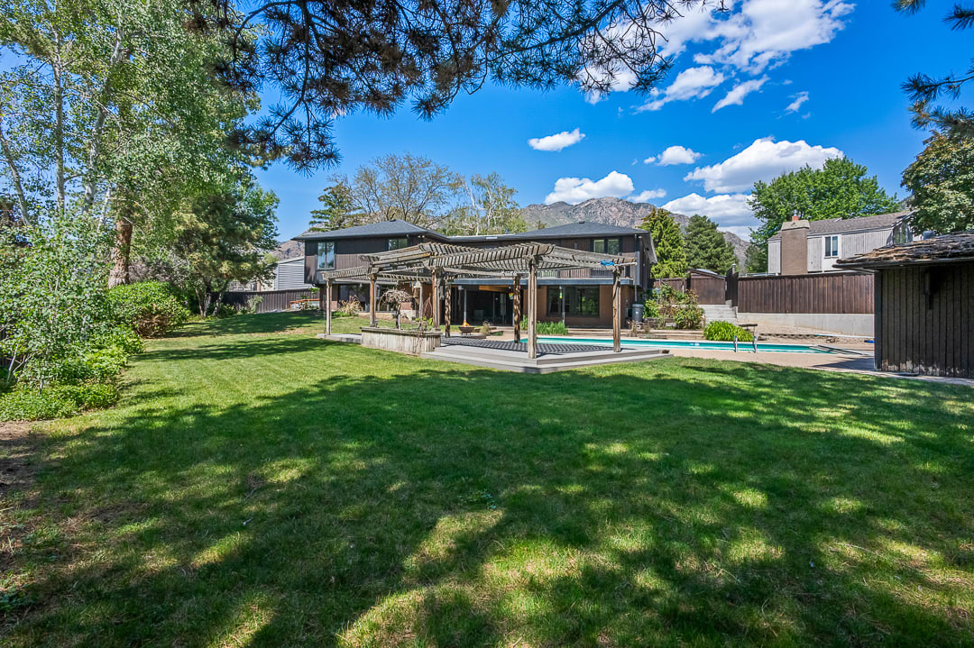 Expansive backyard featuring a manicured lawn, a swimming pool, and an adjacent patio with a wooden pergola