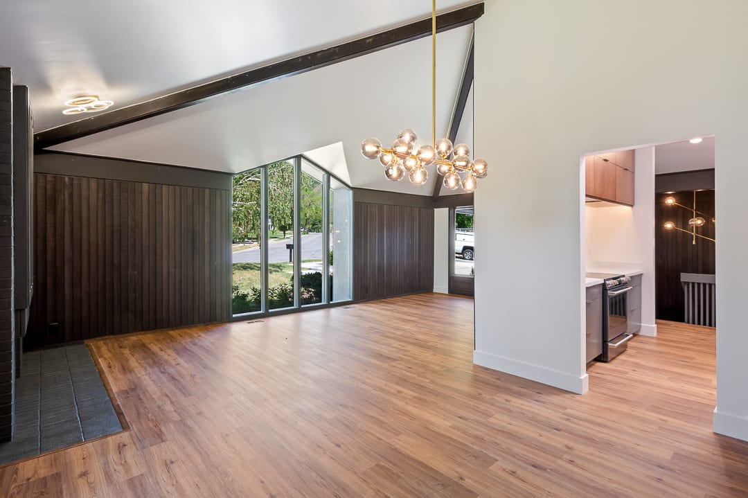 Vaulted ceiling with exposed beams, wood-finish flooring, full-height windows, and a modern chandelier