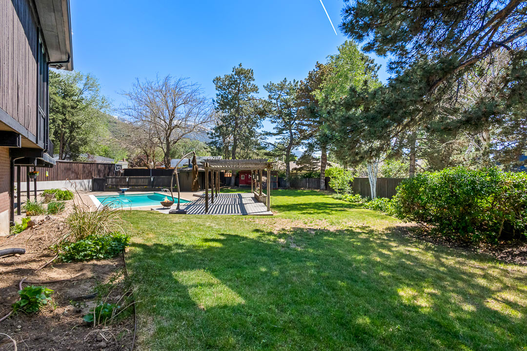 Expansive backyard featuring a swimming pool with paved surround, a wooden pergola, mature trees, and a manicured lawn