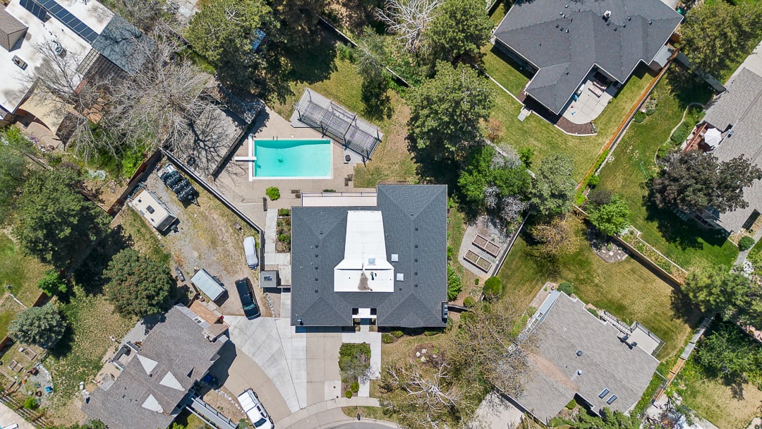 Expansive property featuring a central residence with a dark shingle roof, a rectangular swimming pool with surrounding concrete decking, and multiple raised garden beds