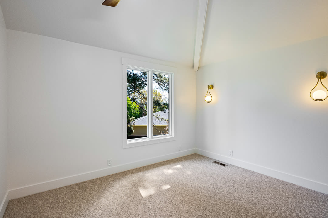 Room featuring vaulted ceilings with exposed beams, two wall-mounted sconces, a large window, and carpet flooring