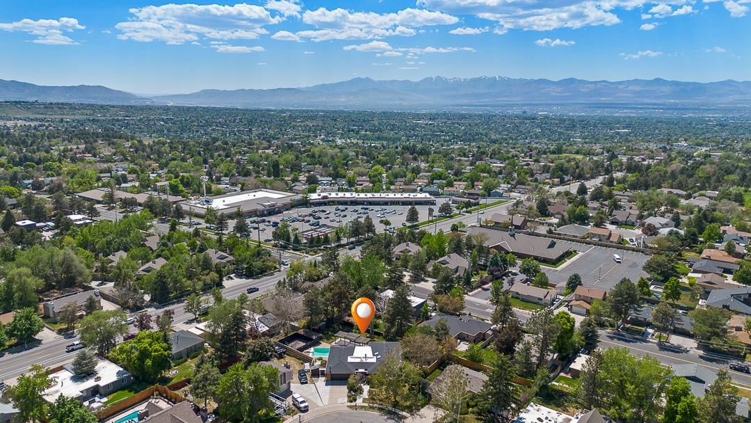 Aerial perspective showcasing a residential area with mature trees, a commercial center, and distant mountains