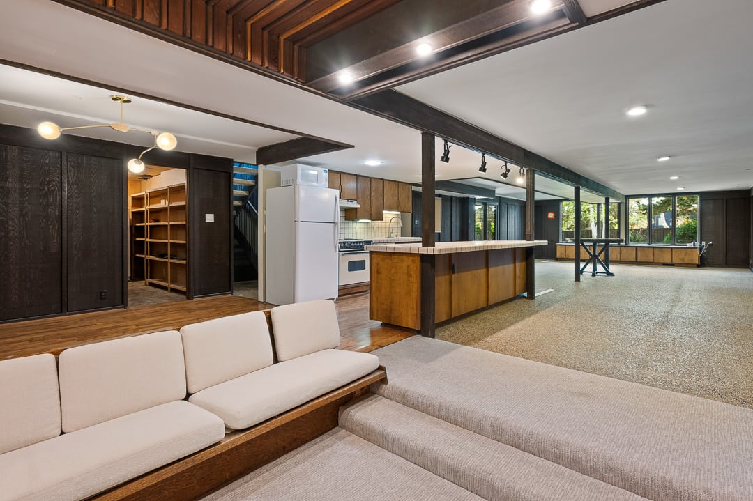 Spacious multi-level interior featuring a built-in sofa, recessed lighting, wood-finish flooring, a kitchen area with wood cabinetry, and large windows