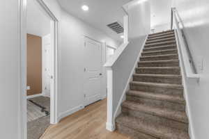 Carpeted staircase with white handrail and baseboards, complemented by wood-finish flooring in the hallway