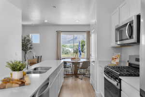 Modern kitchen featuring white shaker cabinetry, stainless steel appliances, light wood-finish flooring, and a spacious island with a double basin sink