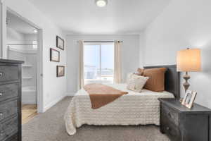 Carpeted bedroom featuring a sliding window, recessed ceiling light, and a white interior door opening to a bathroom with a white tub and shower surround