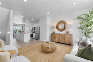 Open-concept living space featuring wood-finish flooring, recessed lighting, and a kitchen with an island, white cabinetry, and stainless steel appliances