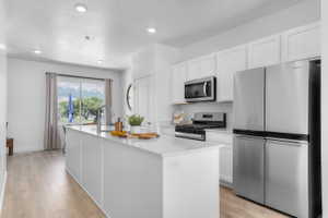 Modern kitchen featuring an expansive island with an integrated sink, stainless steel appliances, crisp white cabinetry, wood-finish flooring, and recessed lighting