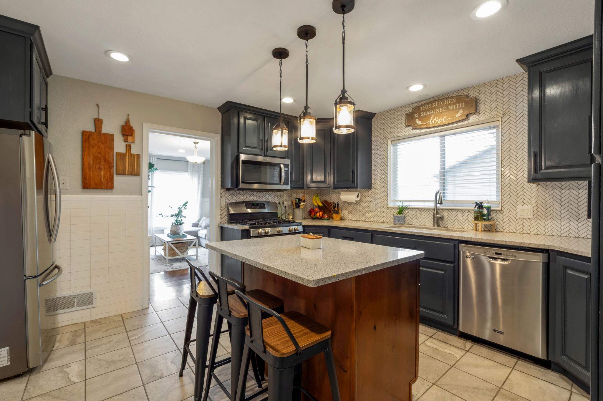 Kitchen featuring dark cabinetry, stainless steel appliances, a center island with a light-toned countertop, herringbone tile backsplash, and recessed lighting