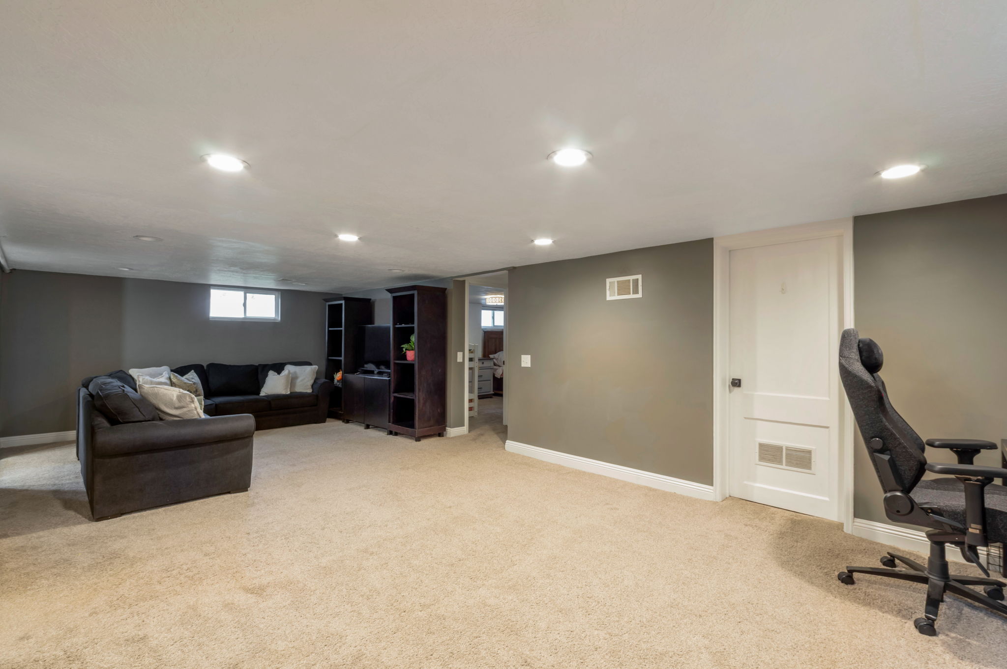 Spacious carpeted room featuring recessed lighting, painted walls, white baseboards, and a white interior door with a paneled design