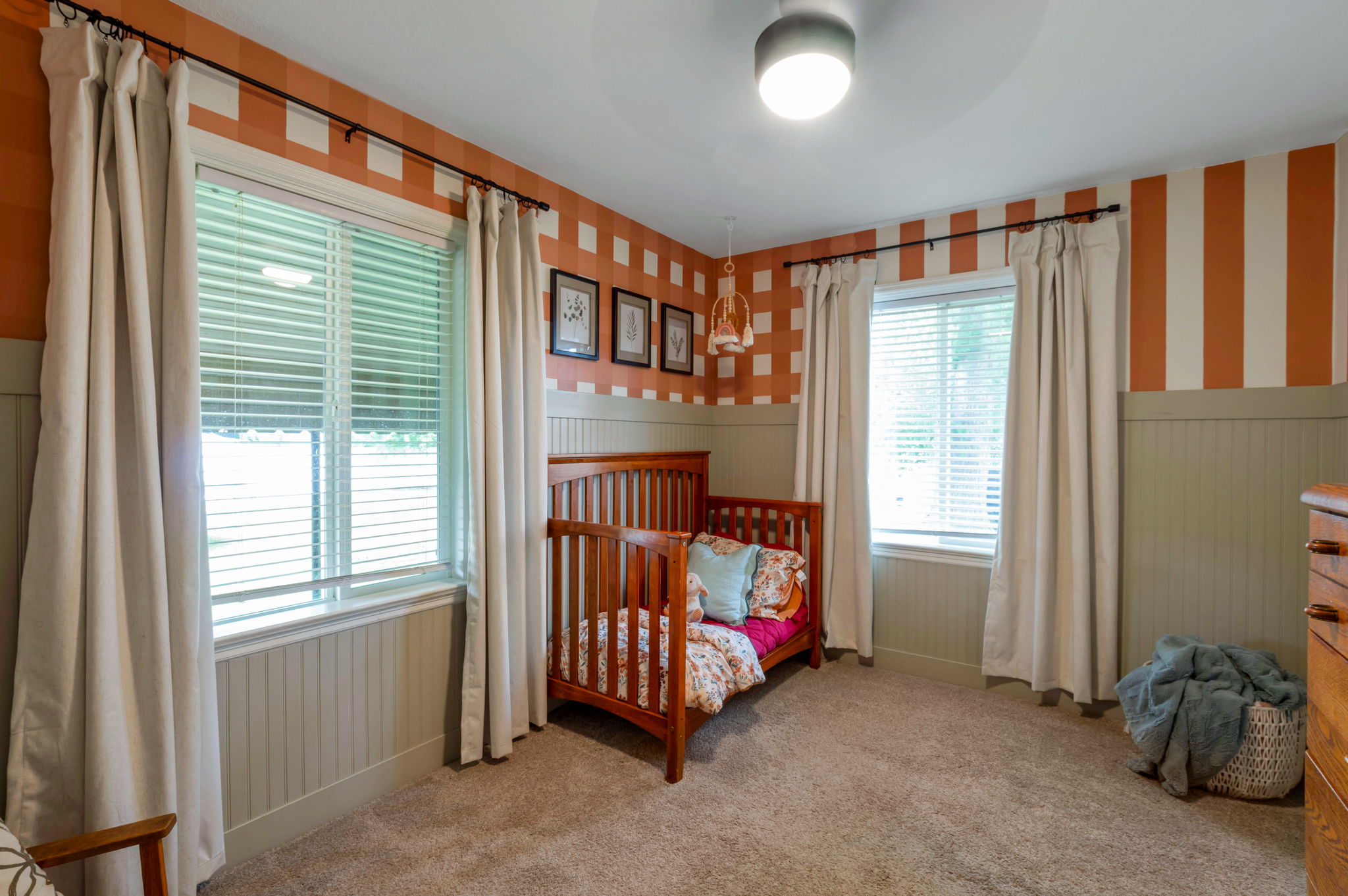 Room featuring two windows with blinds and floor-length drapery, wainscoting, carpet flooring, and a ceiling-mounted light fixture