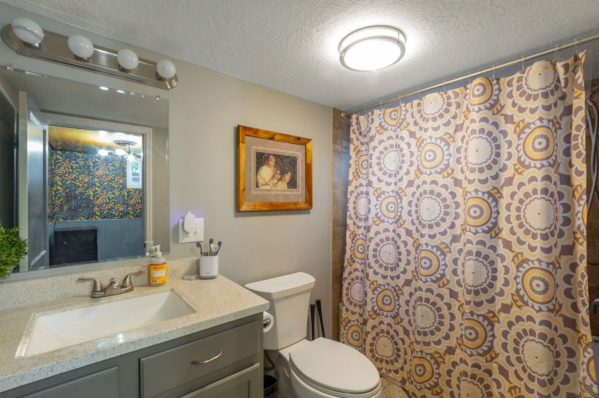 Bathroom featuring a vanity with a light-toned countertop and an integrated sink, a brushed nickel faucet, and a wall-mounted mirror with an overhead light fixture