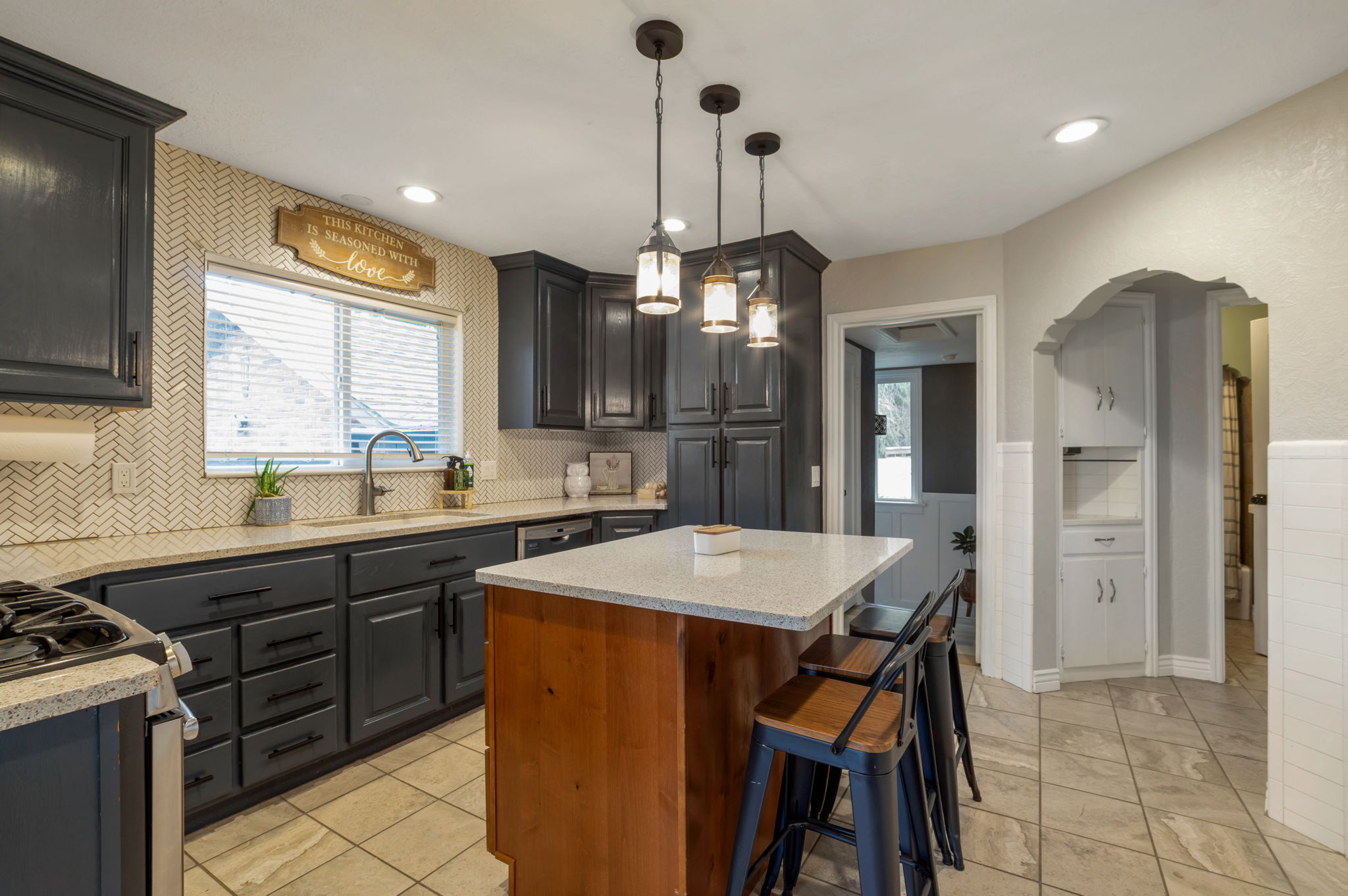 Kitchen featuring dark cabinetry, herringbone-patterned tile backsplash, and light-toned countertops