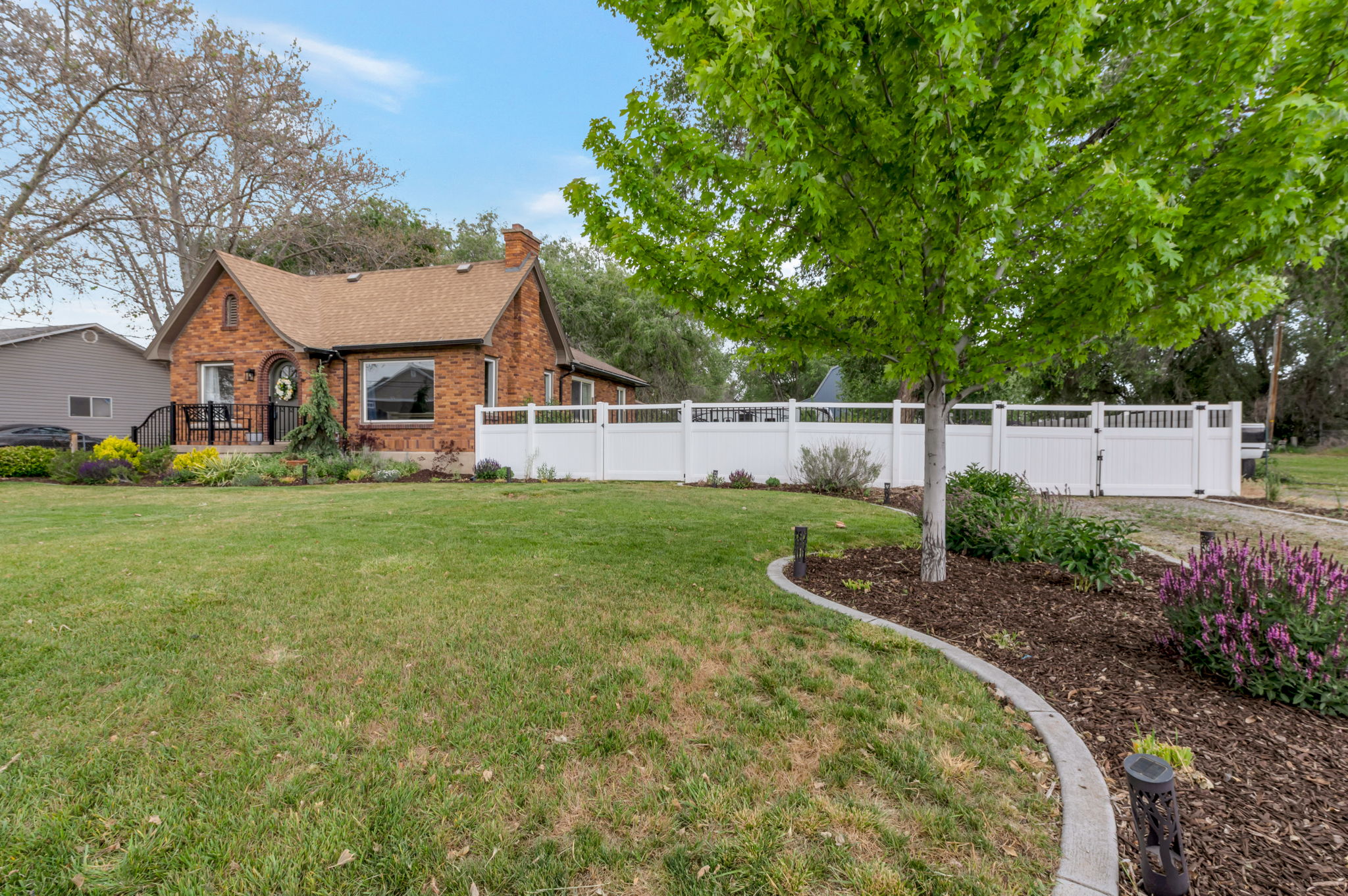 Brick exterior residence featuring a front porch, white fence, and mature landscaping