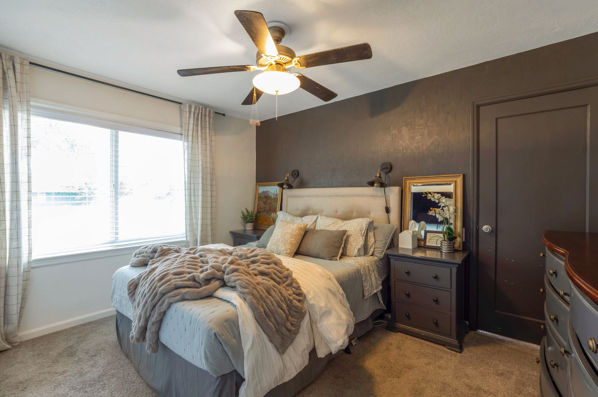 Carpeted room featuring a large window with blinds, a ceiling fan with integrated lighting, a paneled door, and a textured accent wall