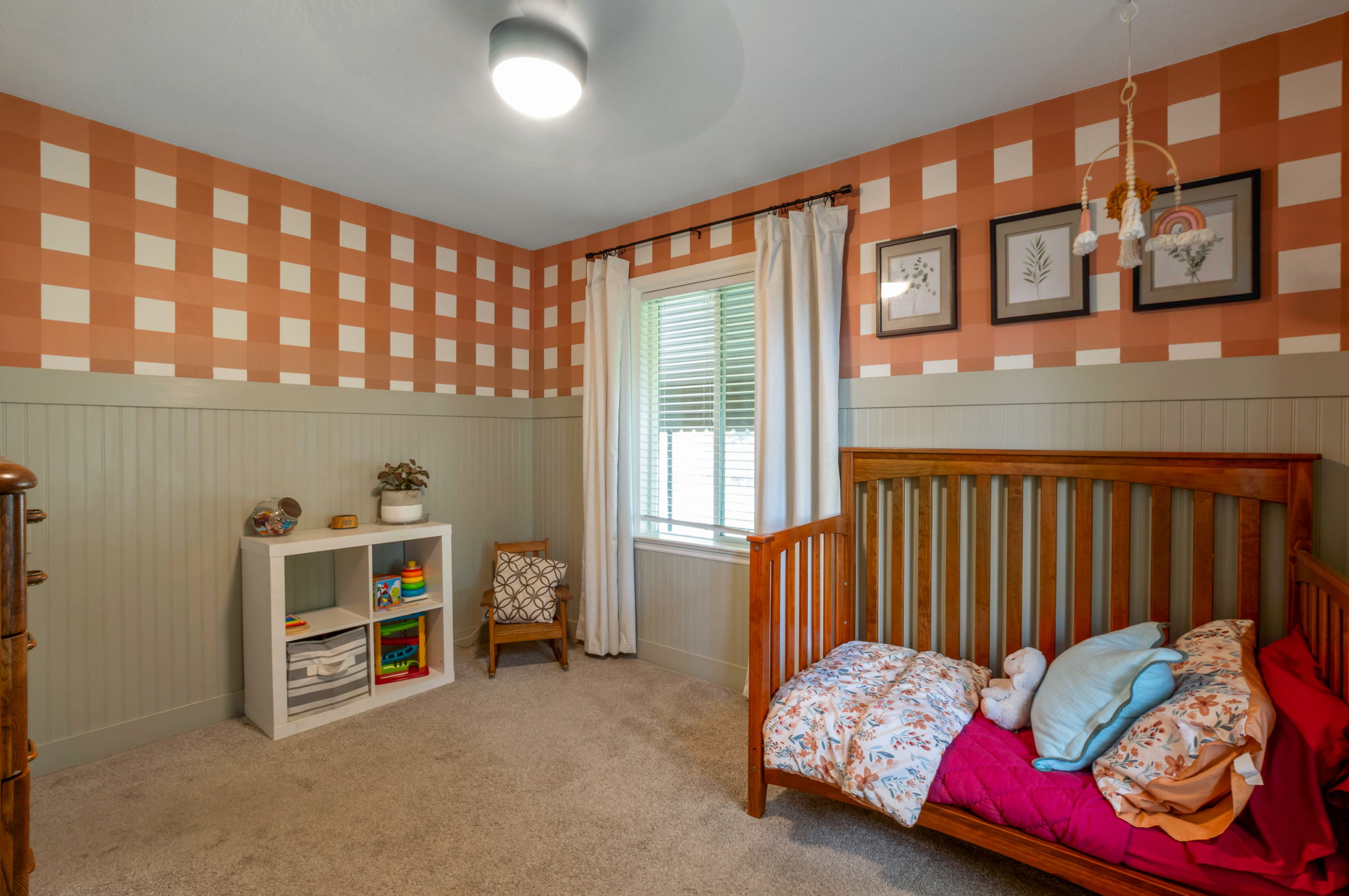 Carpeted room featuring board and batten wainscoting, an accent wall with a checkered pattern, and a window with blinds