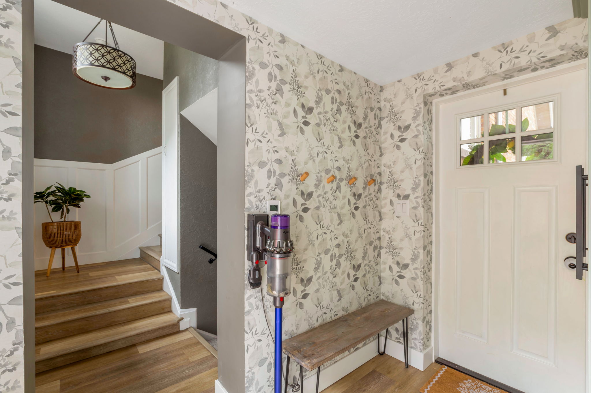 Entryway featuring decorative wallpaper, light wood-finish flooring, and a paneled white door with transom windows
