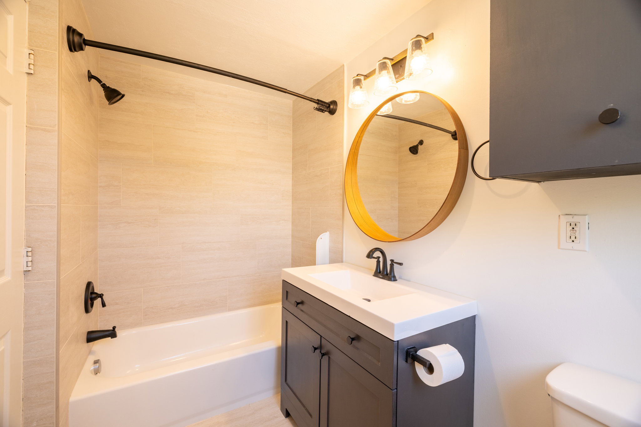 Bathroom featuring a tub/shower combination with light-toned rectangular wall tiling and matte black fixtures