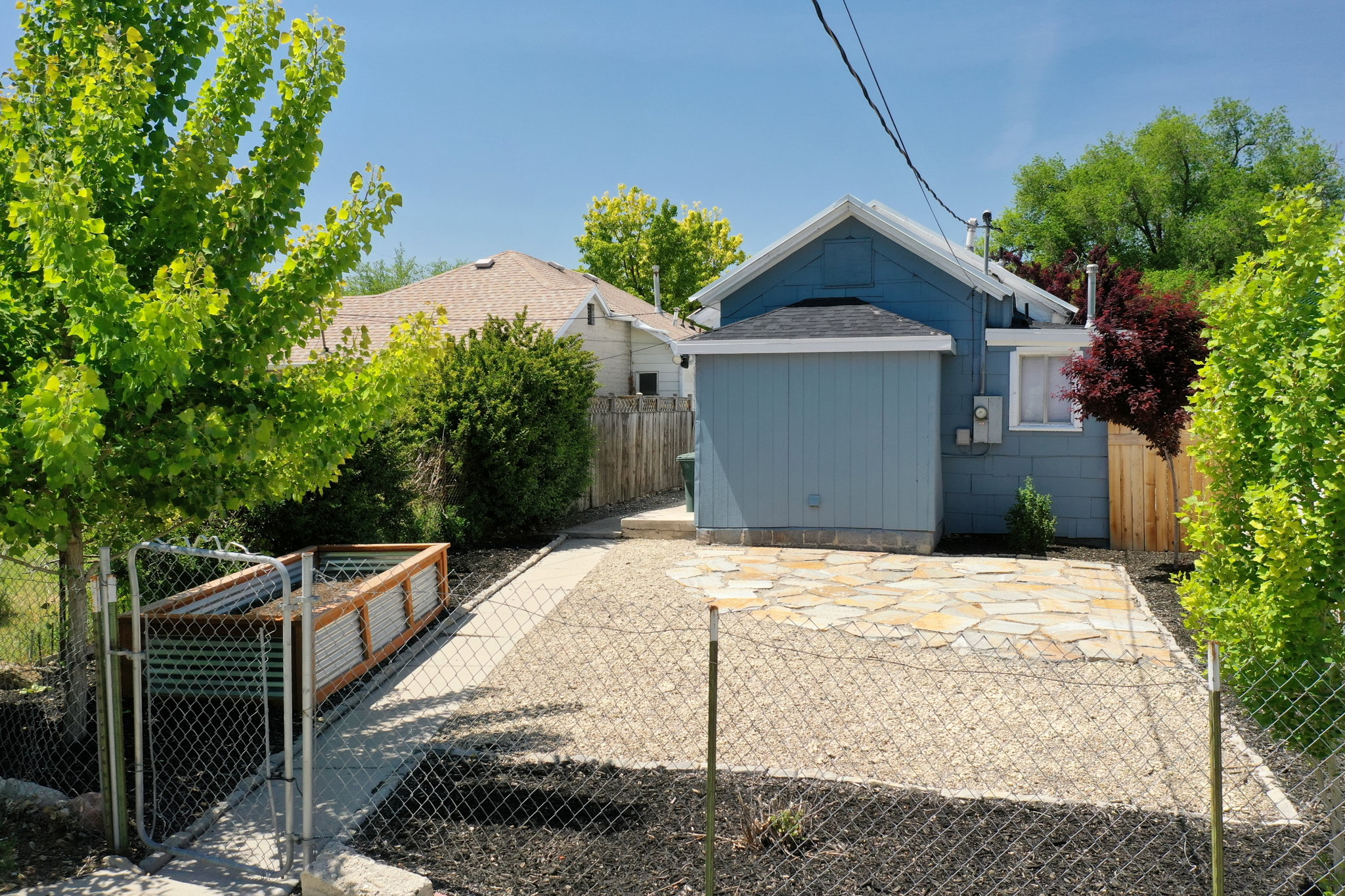 Backyard area featuring a flagstone patio, gravel landscaping, chain-link fencing, and a raised garden bed