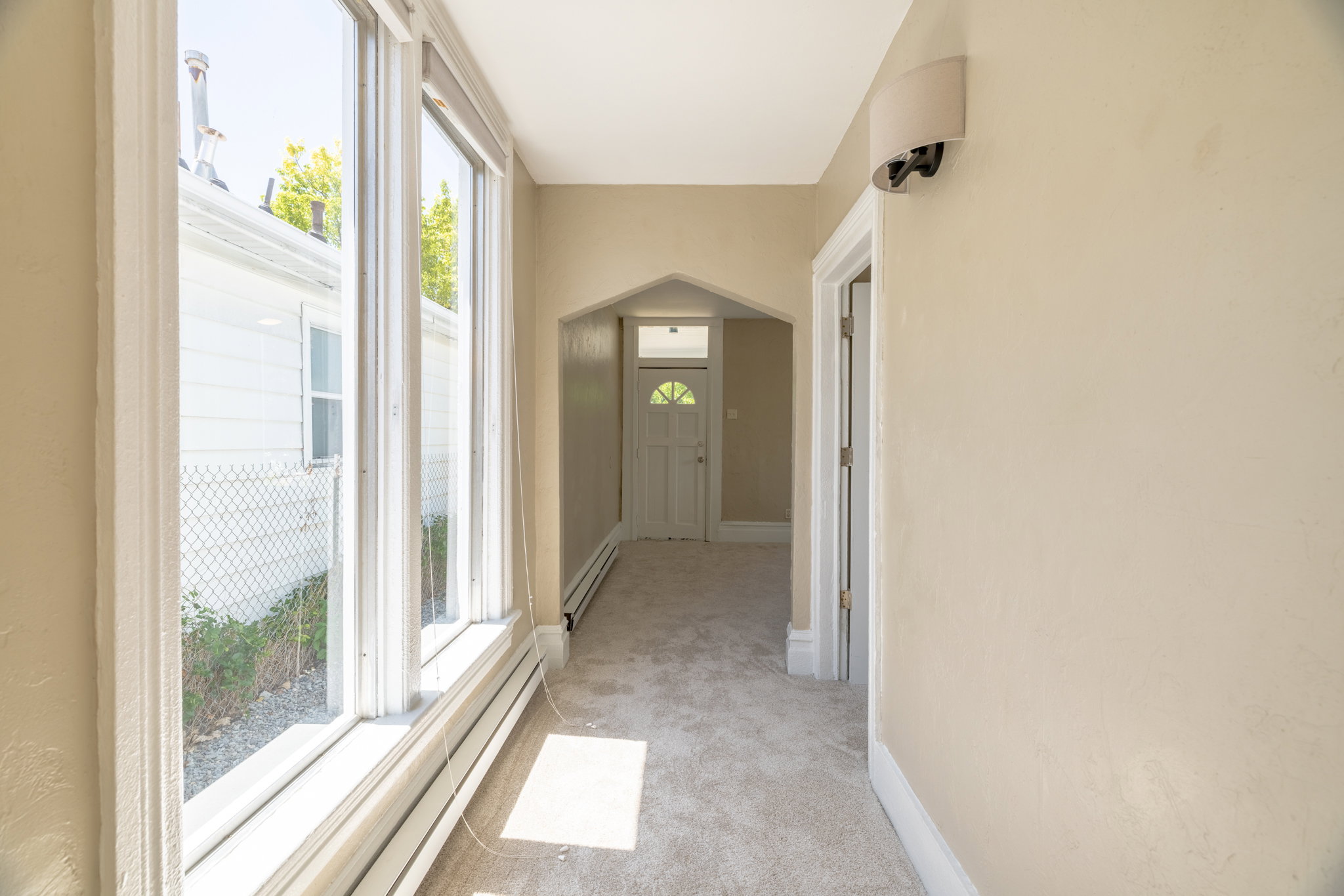 Hallway featuring a wall of multiple windows, light neutral wall paint, carpet flooring, baseboard heating, and an arched entryway