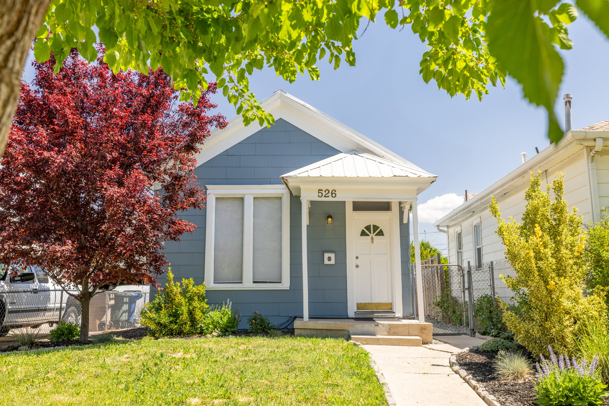 Charming blue exterior featuring a white front door with an arched window, a white metal awning, and a concrete path leading to the entrance