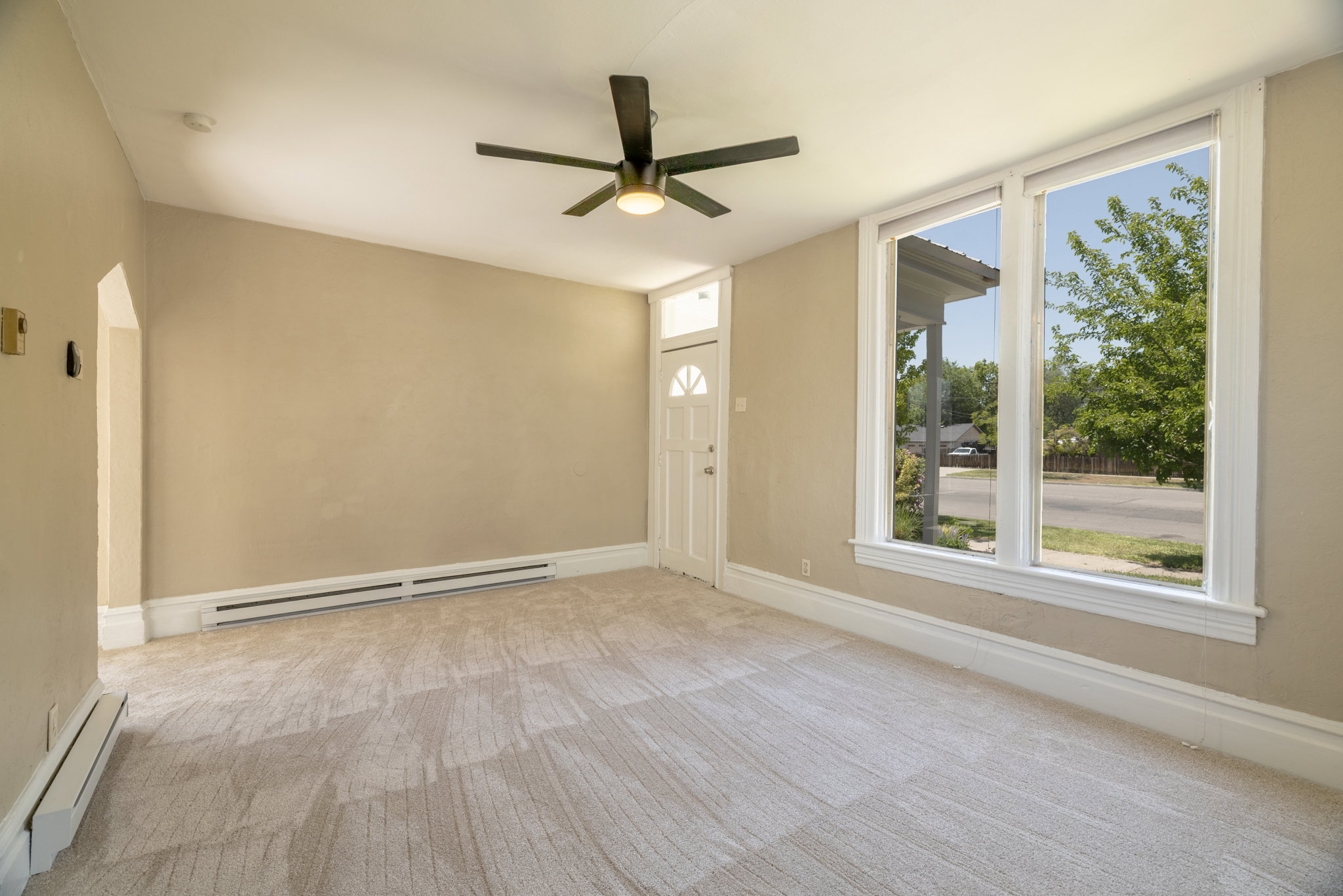 Carpeted living space featuring substantial window framing, a ceiling fan with integrated lighting, and baseboard heating units