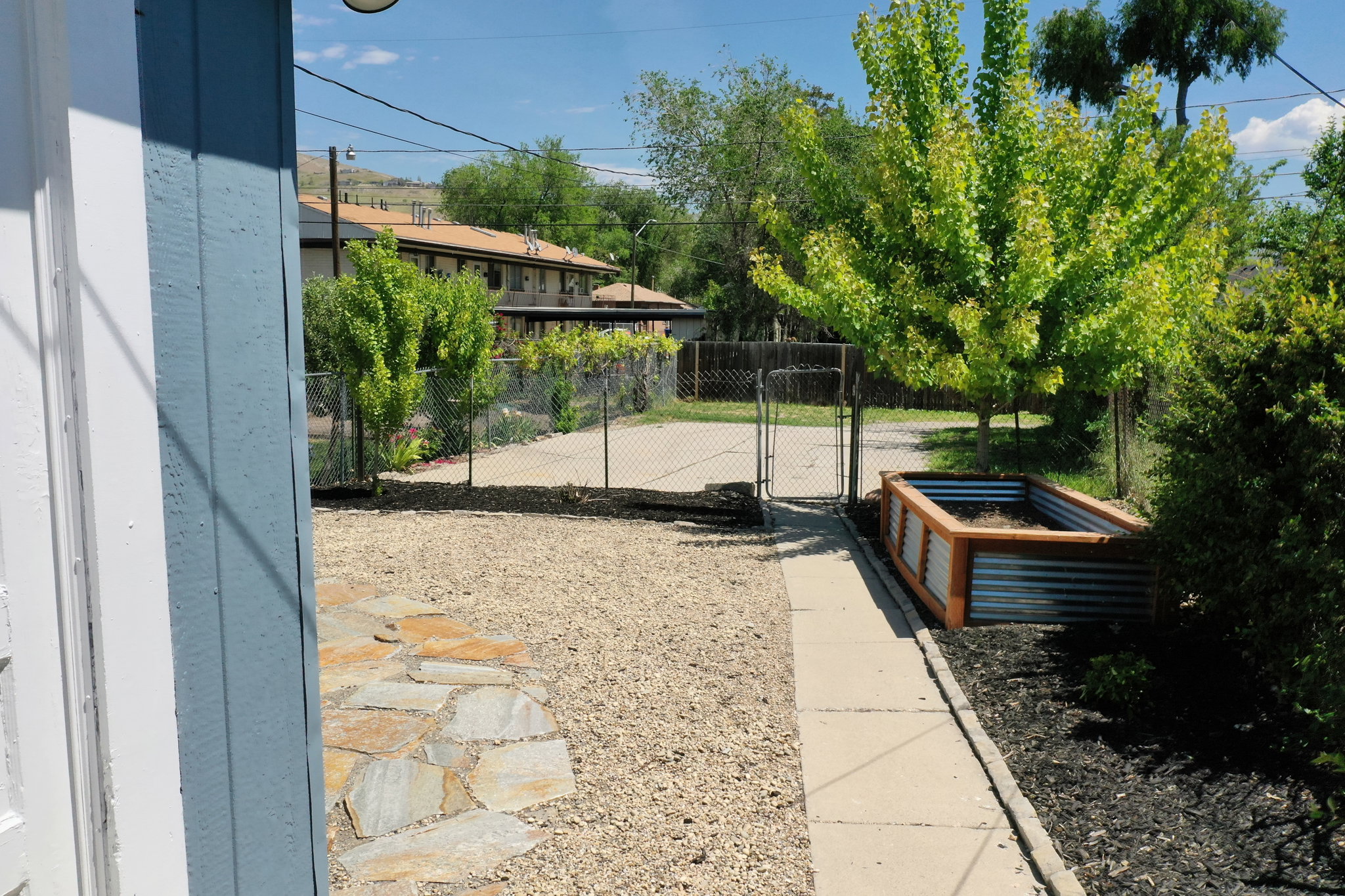 Outdoor space featuring a gravel patio, flagstone pathway, and a large raised garden bed with corrugated metal and wood-finish siding