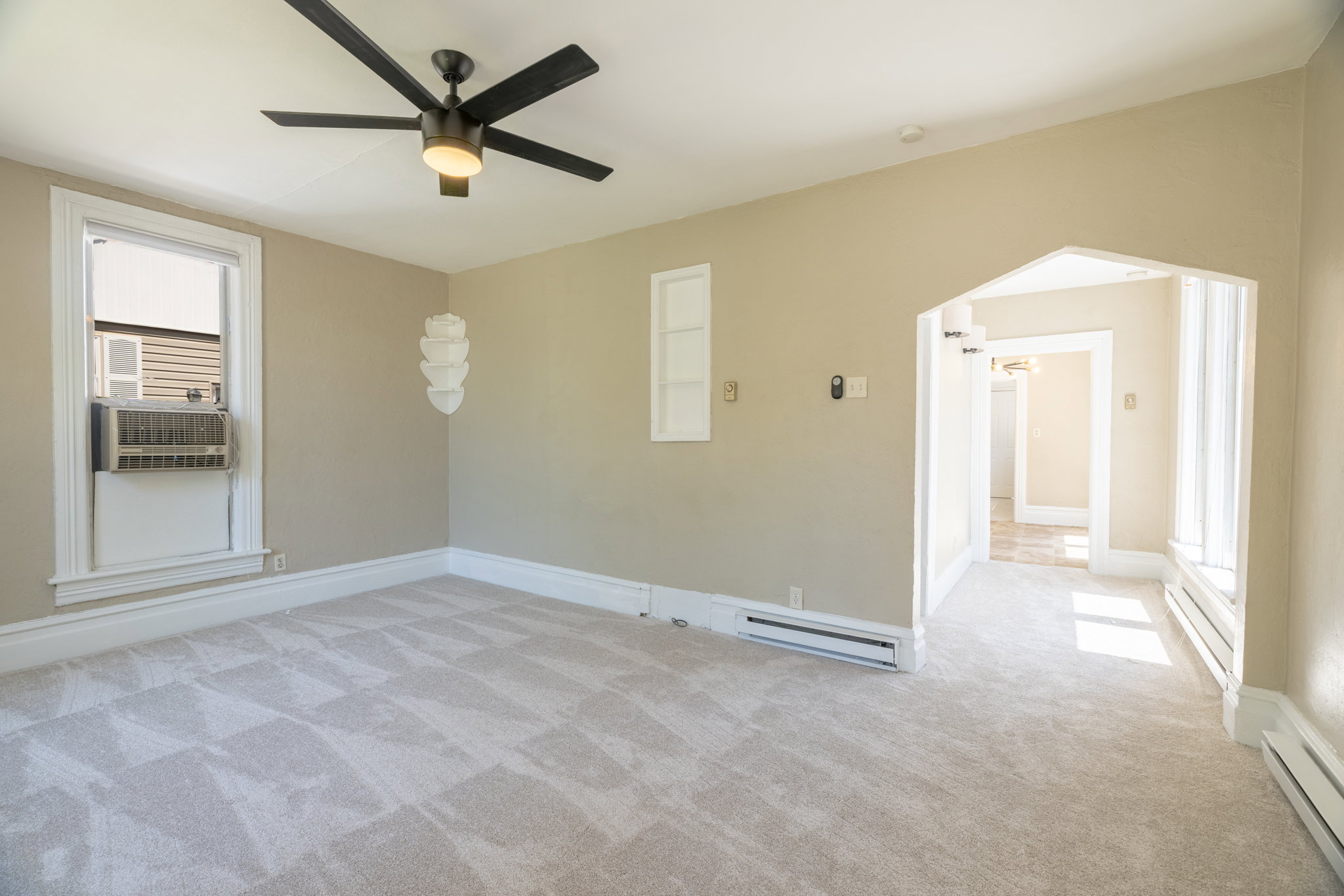 Carpeted room featuring a ceiling fan with integrated lighting, window with white trim, and architectural archway
